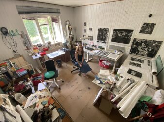 Foto: Gabriela Jolowicz in ihrem Atelier © Gabriela Jolowicz Eine junge Frau in einem bunten Kunstatelier mit Stühlen, Tischen und viel kreativem Material